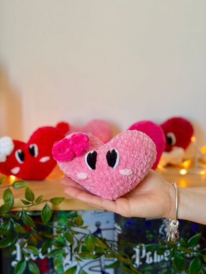 Cœur en métal avec petit nœud rose, bijou élégant de la marque Nuiba, posé sur un fond neutre.